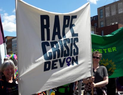 Two women outside with DRCSAS banner at Exeter Pride march
